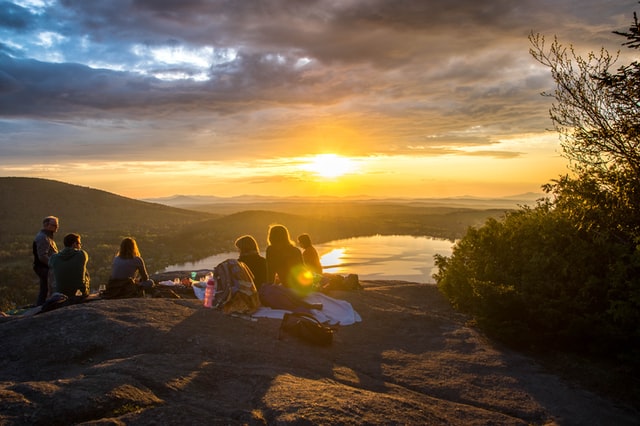 Company Outing; group of people sitting atop a mountain watching the sunset